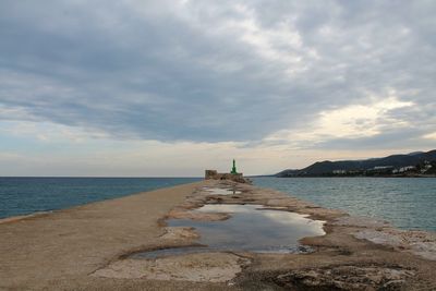 View of lighthouse on beach against cloudy sky