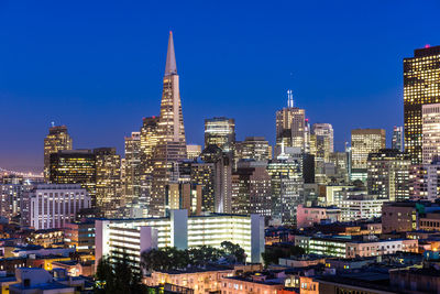 Illuminated buildings in city against blue sky