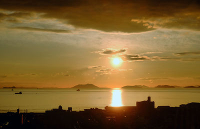 Silhouette buildings by sea against romantic sky at sunset