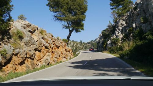 Winding road at tramuntana amidst trees against sky seen through car windshield