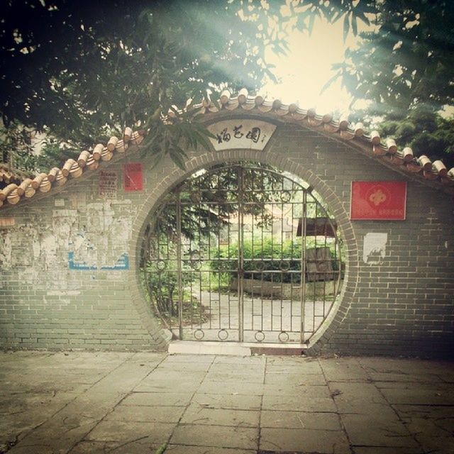 architecture, built structure, arch, tree, building exterior, text, entrance, wall - building feature, gate, day, western script, the way forward, outdoors, door, sunlight, communication, brick wall, footpath, no people, closed