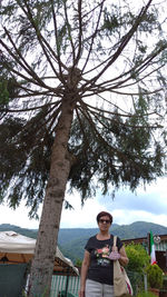 Portrait of young woman standing by tree trunk