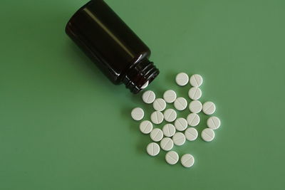 Close-up of pills spilling from bottle against green background