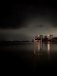 Illuminated buildings by sea against sky at night