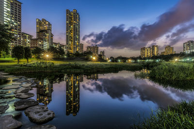 Pond by illuminated city at dusk 