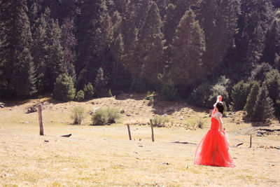 Woman in red gown standing on field at forest