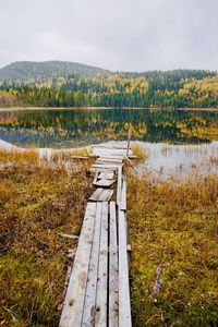 Wooden posts on field by lake against sky