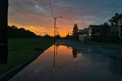 Reflection of buildings on street against sky during sunset