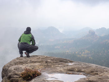 Man sitting at the peak of a mountain on a foggy morning. sit squatting on the peak edge 