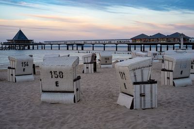 Hooded chairs on beach against sky during sunset