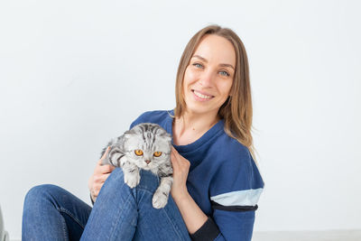 Portrait of smiling young woman holding cat against white background