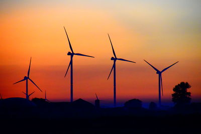 Silhouette wind turbines on field against sky during sunset