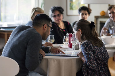 Man reading magazine to girl while sitting with friends and family at dinner party