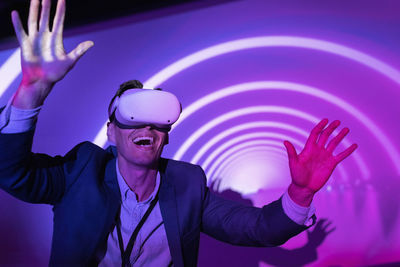 Cheerful businessman watching through futuristic glasses in front of projection screen at convention center