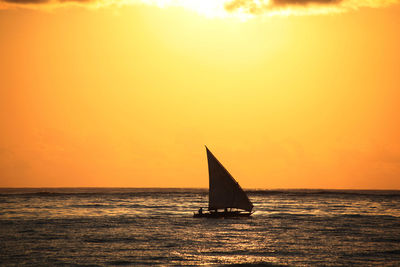 Silhouette sailboat on sea against orange sky