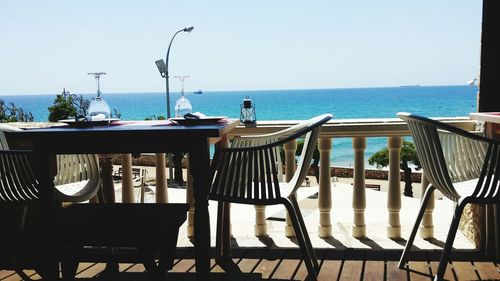 Chairs and table by sea against clear sky