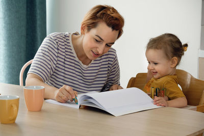 Kids with mother having fun at home by the table, creating hand made art. children drawing and