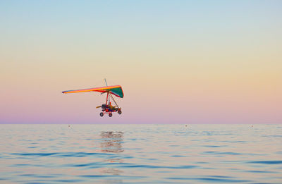 Hang glider over sea against clear sky at dusk