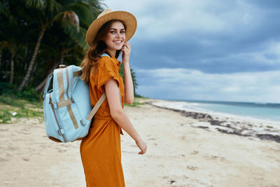 Beautiful young woman standing on beach against sea