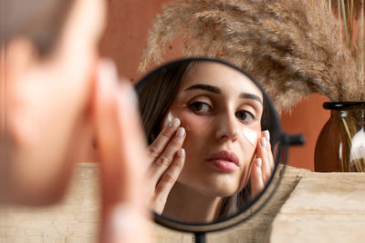 Mirror reflection of woman applying under-eye patch at dressing table closeup