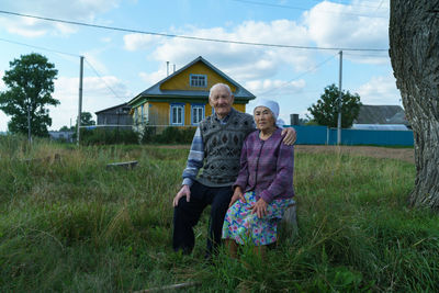Rear view of man and woman sitting on grass against sky