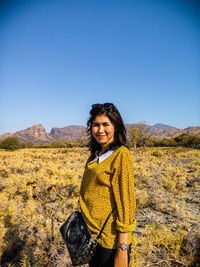 Smiling young woman standing on land against clear sky