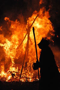 Silhouette of man standing by fire at night