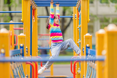 A little girl hangs on a childrens ladder on a bright playground in the park in summer