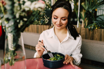 Happy young vegetarian woman eats healthy vegan food green salad sitting in a restaurant