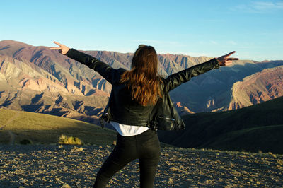 Rear view of woman with arms outstretched standing on landscape against mountain range