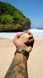 Close-up of hand holding sand at beach against sky