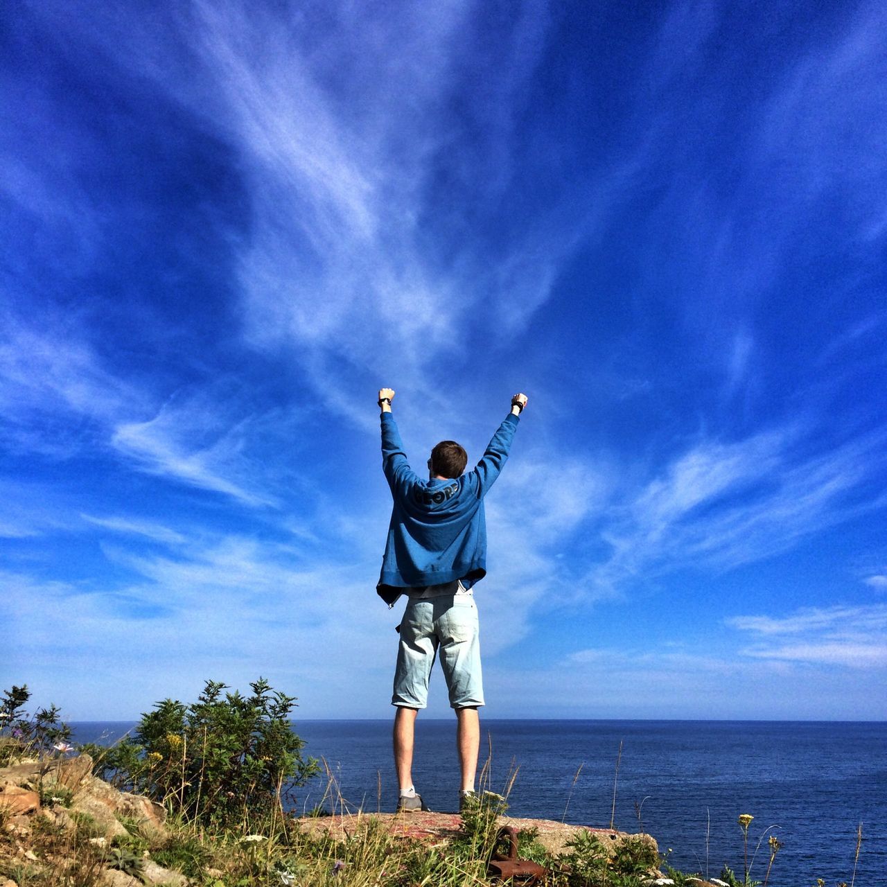 full length, sky, leisure activity, lifestyles, casual clothing, standing, arms raised, blue, sea, cloud - sky, arms outstretched, water, freedom, jumping, horizon over water, tranquility, cloud, tranquil scene