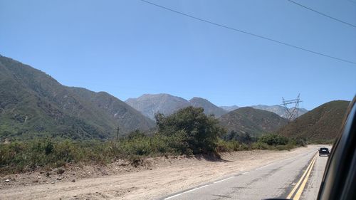 Road leading towards mountains against clear blue sky