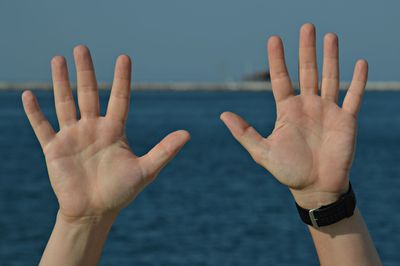 Cropped image of person showing stop gesture against sea and sky