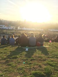 Rear view of people sitting on shore against sunset sky