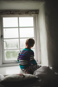 Rear view of boy looking through window at home