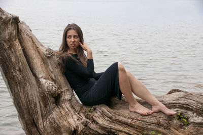 Portrait of young woman sitting on wood against sea