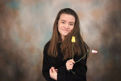 Portrait of smiling woman holding roses while standing against backdrop