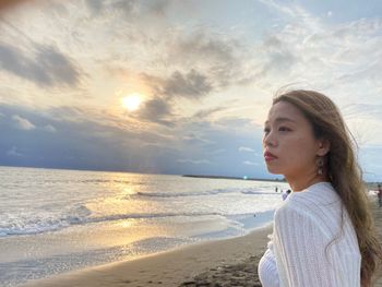 Young woman looking at sea against sky during sunset