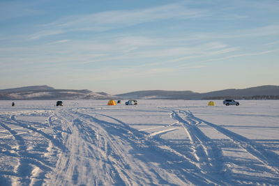 Trace from cars on a snowy big lake with fishermen in the background.