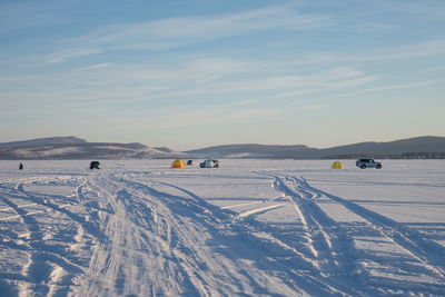 Trace from cars on a snowy big lake with fishermen in the background.