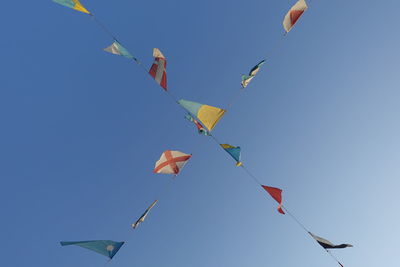 Low angle view of flags hanging against clear blue sky