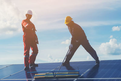 Low angle view of male technicians working on solar panels against sky