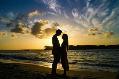 Silhouette couple standing at beach against sky during sunset