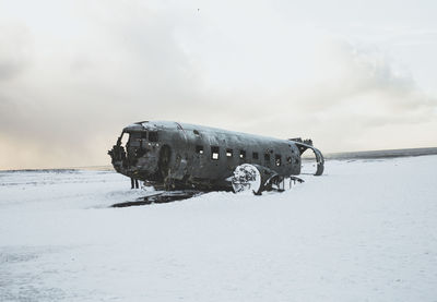 Abandoned airplane on snow covered landscape against sky