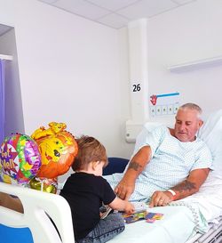 Grandfather and grandson playing with toys on bed in hospital ward