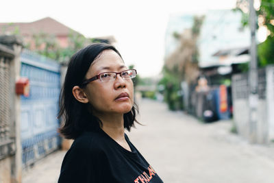 Portrait of young woman looking away while standing on street in city