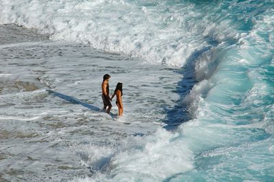 High angle view of couple holding hands while standing on shore at beach