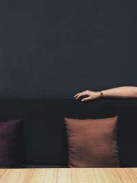 Cropped hand of woman on sofa against wall