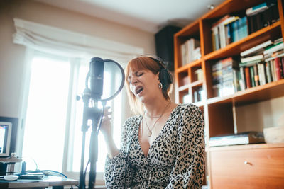 Female vocalist in headset singing song into mic with pop filter during record process at home
